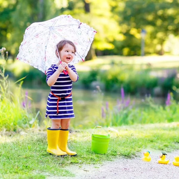 Cute little kid girl in yellow rainboots in summer park — Stock Photo, Image