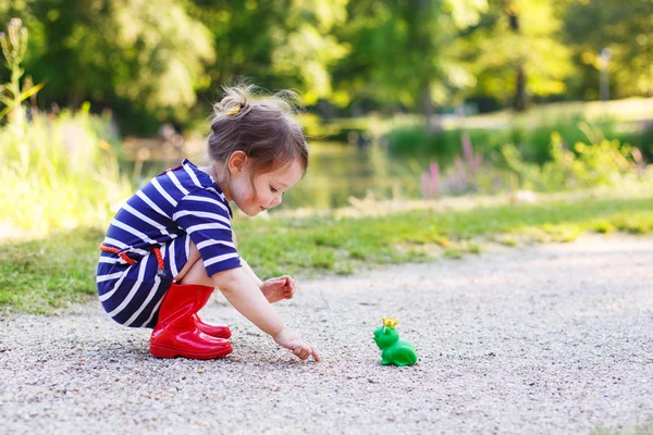 Belle petite fille en bottes de pluie rouge jouant avec grenouille en caoutchouc — Photo