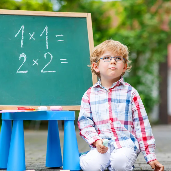 可爱的小小孩男孩戴着眼镜在黑板练习立体几何 — 图库照片