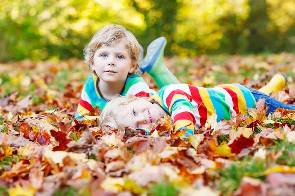 Dois meninos pequenos que põem em folhas de outono na roupa colorida — Fotografia de Stock