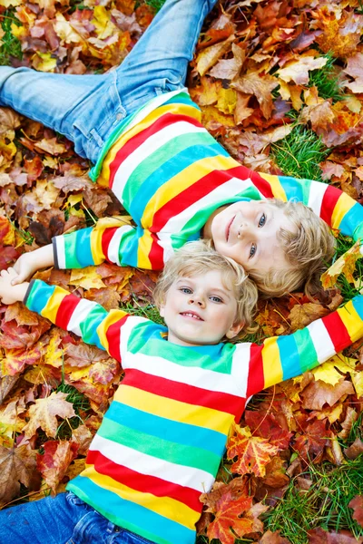 Two little kid boys laying in autumn leaves in colorful clothing — Stock Photo, Image