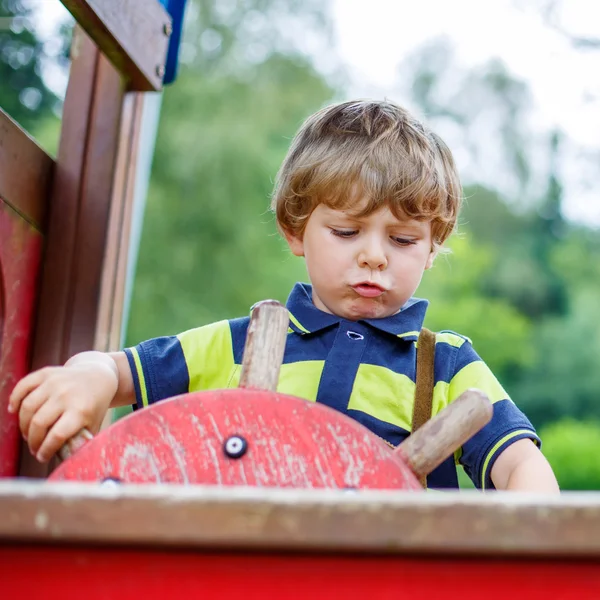 Niño niño finge conducir un coche imaginario en el parque infantil — Foto de Stock