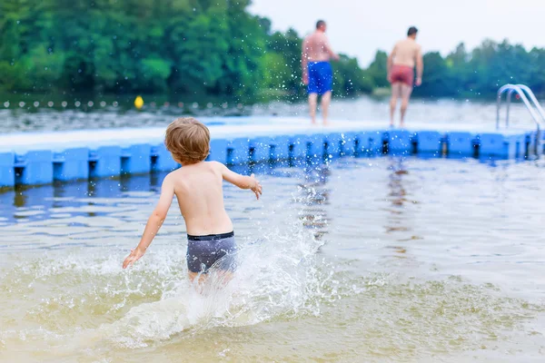 Pequeño chico rubio divirtiéndose con salpicaduras en un lago, outdoo — Foto de Stock