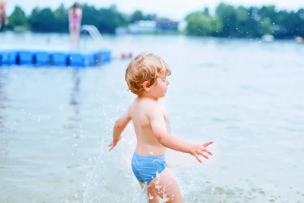 Pequeño chico rubio divirtiéndose con salpicaduras en un lago, outdoo — Foto de Stock