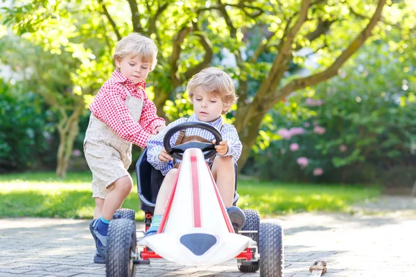 Dos hermanitos jugando con un coche de pedal en el jardín de su casa —  Fotos de Stock