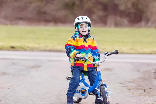 Niño en casco de seguridad y colorido impermeable bicicleta de montar, outd —  Fotos de Stock