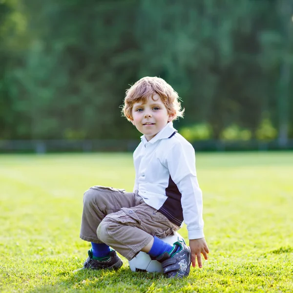 Blond boy of 4 resting with football on football field — Stock Photo, Image