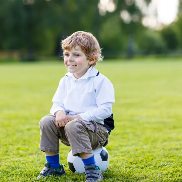Blond boy of 4 resting with football on football field — Stock Photo, Image