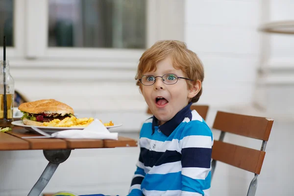 Kleine jongen eten fastfood: Franse frietjes en hamburger — Stockfoto