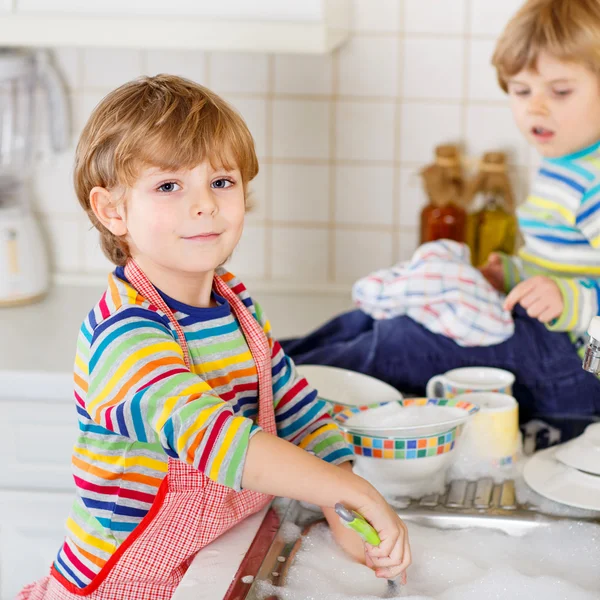 Два маленьких смешных помощника на кухне с мытьем посуды — стоковое фото