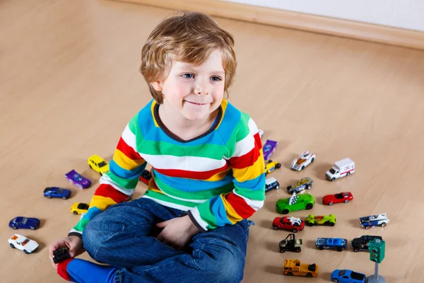 Забавный маленький мальчик играет с кучей игрушечных машин в помещении — стоковое фото