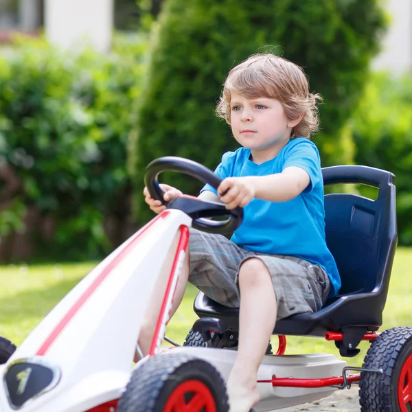 Pequeño niño activo que se divierte y conduce coche de carreras de juguetes — Foto de Stock