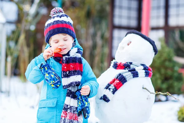 Funny kid boy i färgglada kläder att göra en snögubbe, utomhus — Stockfoto