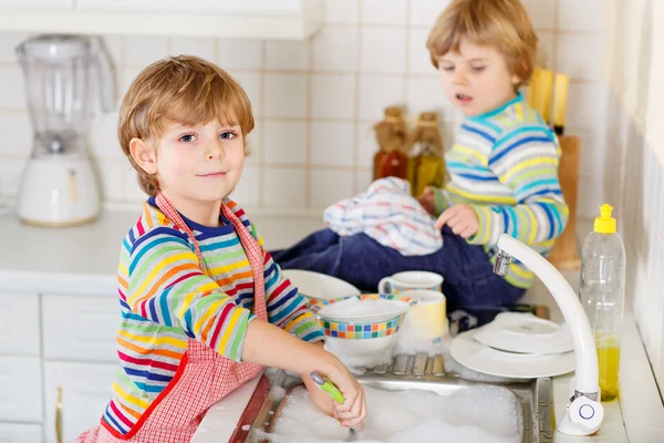 Два маленьких смешных помощника на кухне с мытьем посуды — стоковое фото