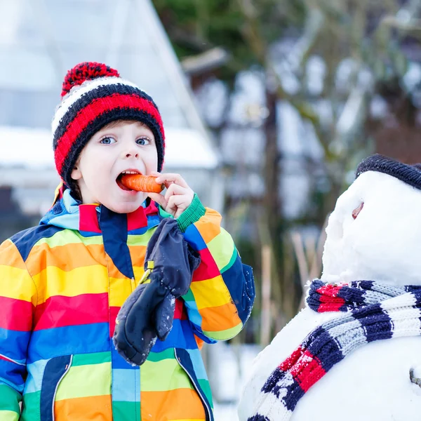 Grappige kind jongen in kleurrijke kleding maken een sneeuwpop, buitenshuis — Stockfoto