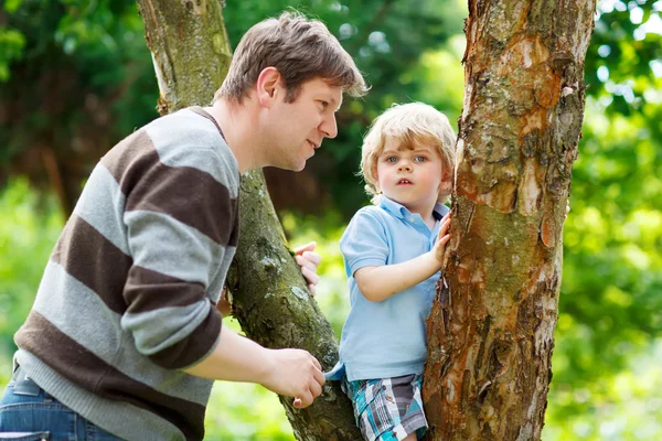 Cute little kid boy enjoying climbing on tree with father, outdo — Stock Photo, Image