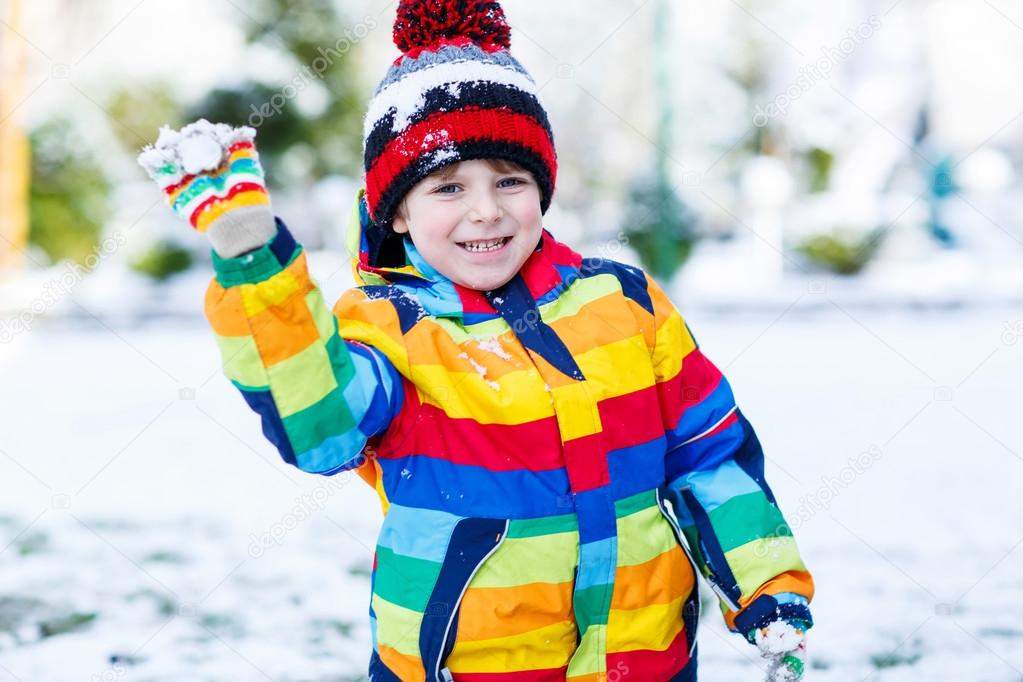 Little  boy in colorful winter clothes playing with snowman, out