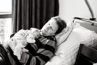 Yeni doğmuş bebeğini kucağında tutan mutlu bir baba. Şirin küçük bebek evde babasının göğsünde huzur içinde uyuyor. Aile sevgisi, bağlılık ve ebeveynlik kavramı