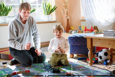 Baba ve oğul yarış arabalarıyla yarış pistinde, kapalı alanda, arabalarla oynuyorlar. Küçük mutlu anaokulu çocuğu ve genç adam kapalı alandaki yarış oyunlarıyla eğleniyor.