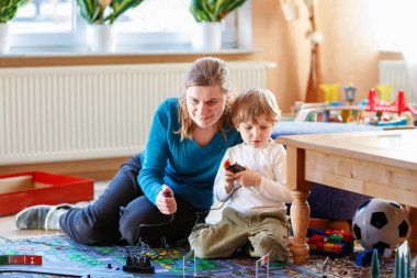 Anne ve oğlu yarış arabalarıyla yarış pistinde, kapalı alanda, arabalarla oynuyorlar. Küçük mutlu anaokulu çocuğu ve genç kadın kapalı alandaki yarış oyunlarıyla eğleniyorlar.