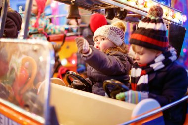 Sevimli küçük erkek ve kız, Noel funfair veya pazar, açık havada bir atlıkarınca üzerinde kardeşler. Mutlu çocuklar, arkadaşlar eğleniyor. Bir çocuğa seçici bir odaklanma. Tatil, çocuklar, yaşam tarzı kavramı.