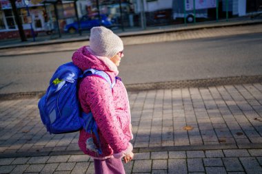 Küçük kız büyük bir çantayla okuldan eve yürüyor.