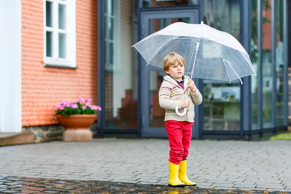 Pequeño niño rubio caminando con un gran paraguas al aire libre — Foto de Stock