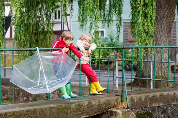 Два маленьких мальчика с большим зонтиком на улице — стоковое фото