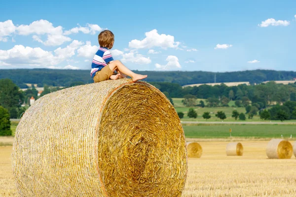 Malý chlapec dítě sedí na balíku sena v létě — Stock fotografie