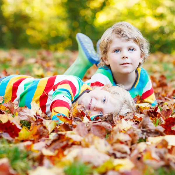 Two little kid boys laying in autumn leaves in colorful clothing — Stock Photo, Image