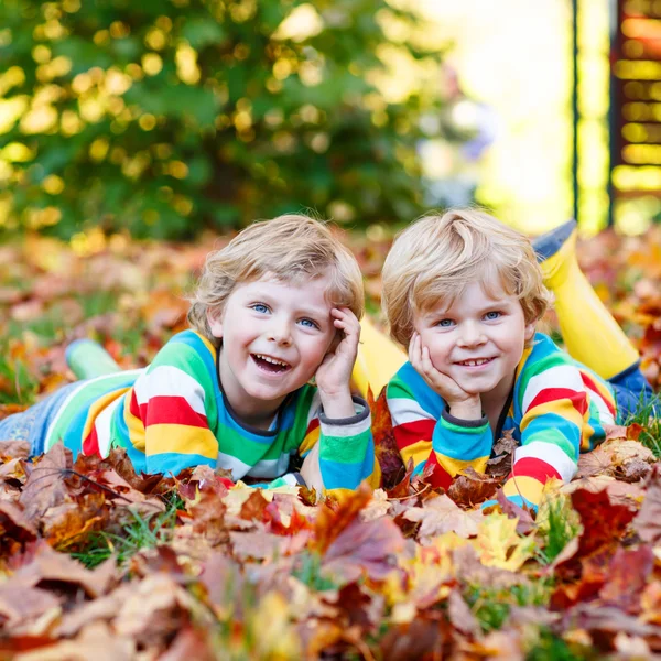 Two little kid boys laying in autumn leaves in colorful clothing — Stock Photo, Image