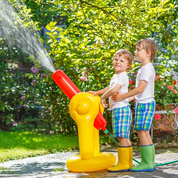 Due bambini piccoli che giocano con tubo da giardino e acqua in estate — Foto Stock