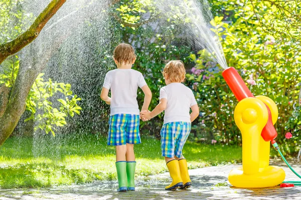 Twee kleine kinderen spelen met tuinslang in de zomer — Stockfoto