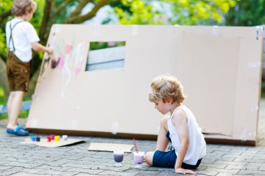 Two little kid boys painting big paper house with colorful paint