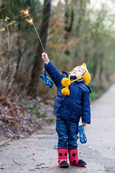 Little child in winter clothes holding burning sparkler — Stock Photo, Image