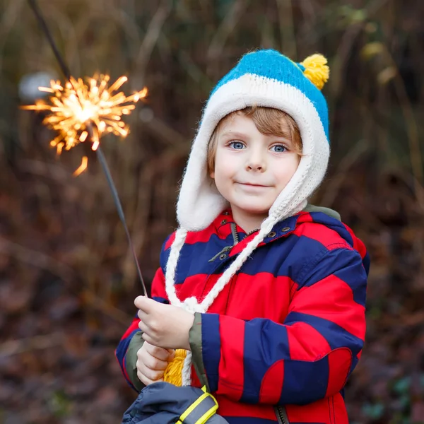 Little child in winter clothes holding burning sparkler — 图库照片