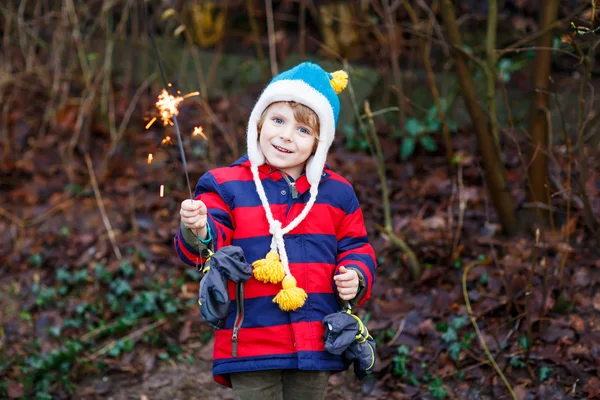 Little child in winter clothes holding burning sparkler