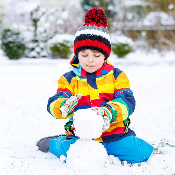 Menino pré-escolar engraçado em roupas coloridas fazendo um boneco de neve — Fotografia de Stock