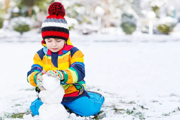 Lovely little boy in colorful clothes making a snowman — Stock Photo, Image