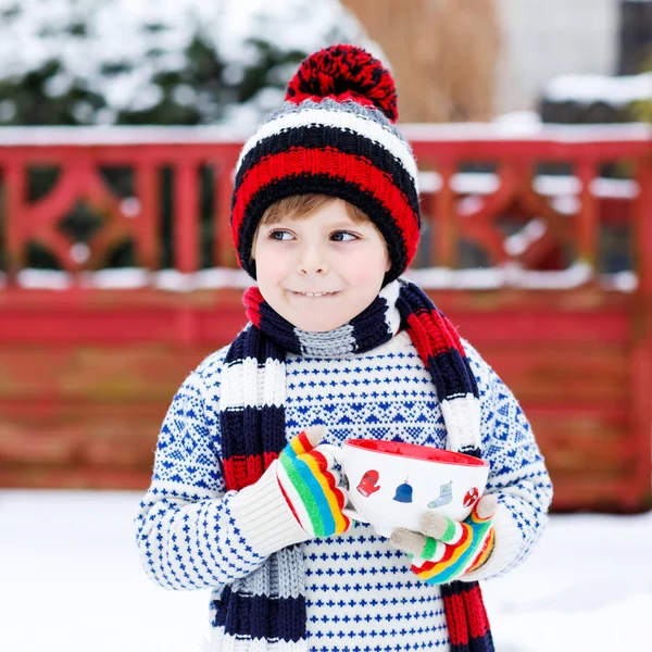 雪の結晶とホットチョコと大きなカップを保持している面白い小さな子供 — ストック写真