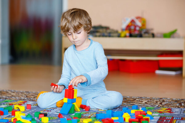 Little blond child playing with colorful wooden blocks indoor