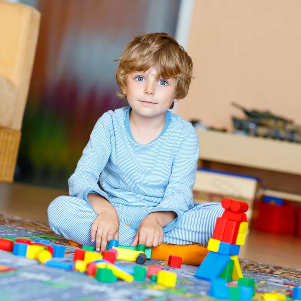 Piccolo bambino biondo che gioca con blocchi di legno colorati al coperto — Foto Stock