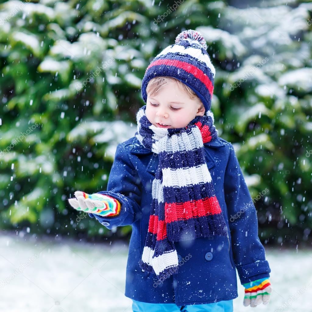 Cute little funny boy in colorful winter clothes having fun with