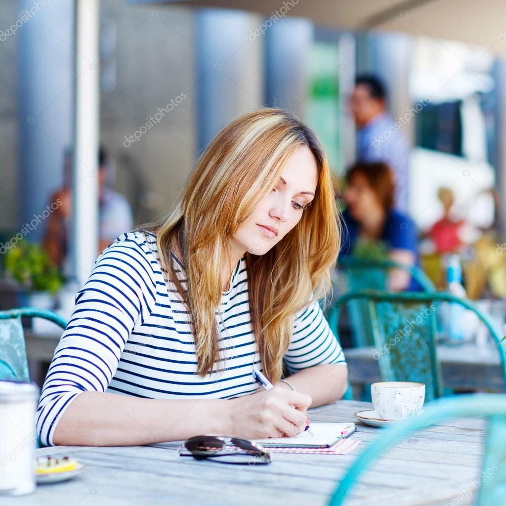 Woman drinking coffee and writing notes in cafe