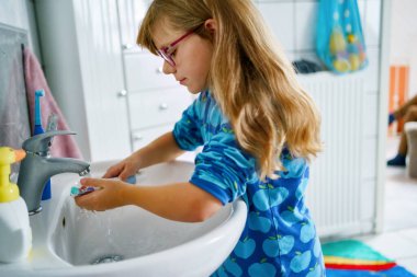 Küçük kız banyoda sabah rutini yapıyor. Çocuk dişlerini fırçalıyor, yüzünü yıkıyor, saçlarını tarıyor..