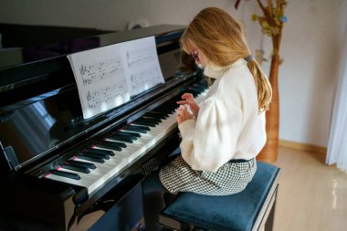 Evde piyano çalan küçük bir kız. Mutlu çocuk müzik aleti çalıyor..