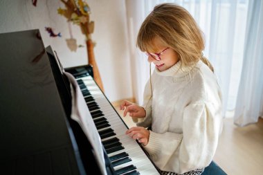 Evde piyano çalan küçük bir kız. Mutlu çocuk müzik aleti çalıyor..