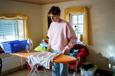 Genç çocuk evde ütüyle çamaşır yıkıyor ve ütülüyor..