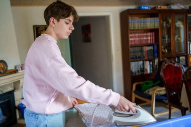 Genç çocuk evde ütüyle çamaşır yıkıyor ve ütülüyor..