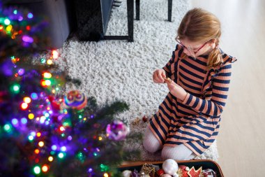Küçük liseli kız geleneksel Noel ağacını evde eski süslemeler ve oyuncaklarla süslüyor..